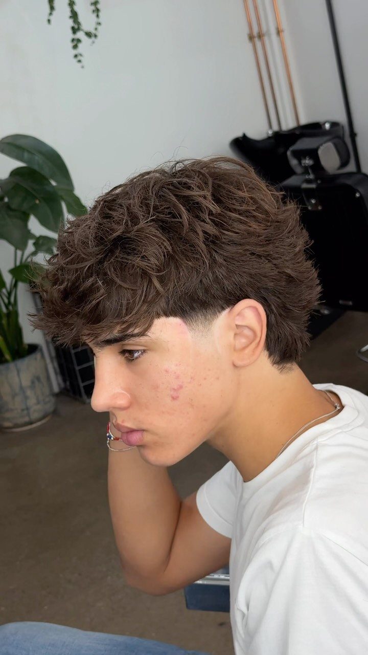 Young man with textured brown hair and a medium fade haircut in profile.