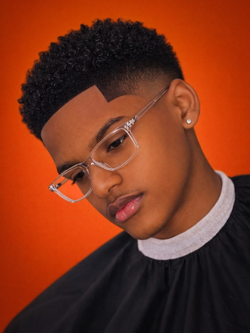 Young man with tightly coiled hair and a taper fade wearing clear glasses.