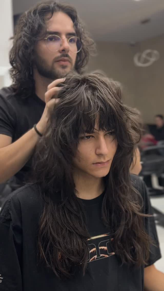 Man with a layered wolf cut hairstyle being styled by a professional barber.