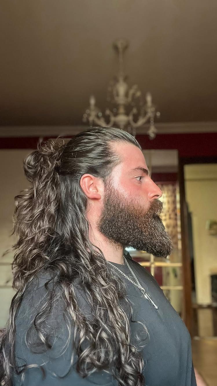 Man with a long curly beard and half-up bun hairstyle with flowing locks.