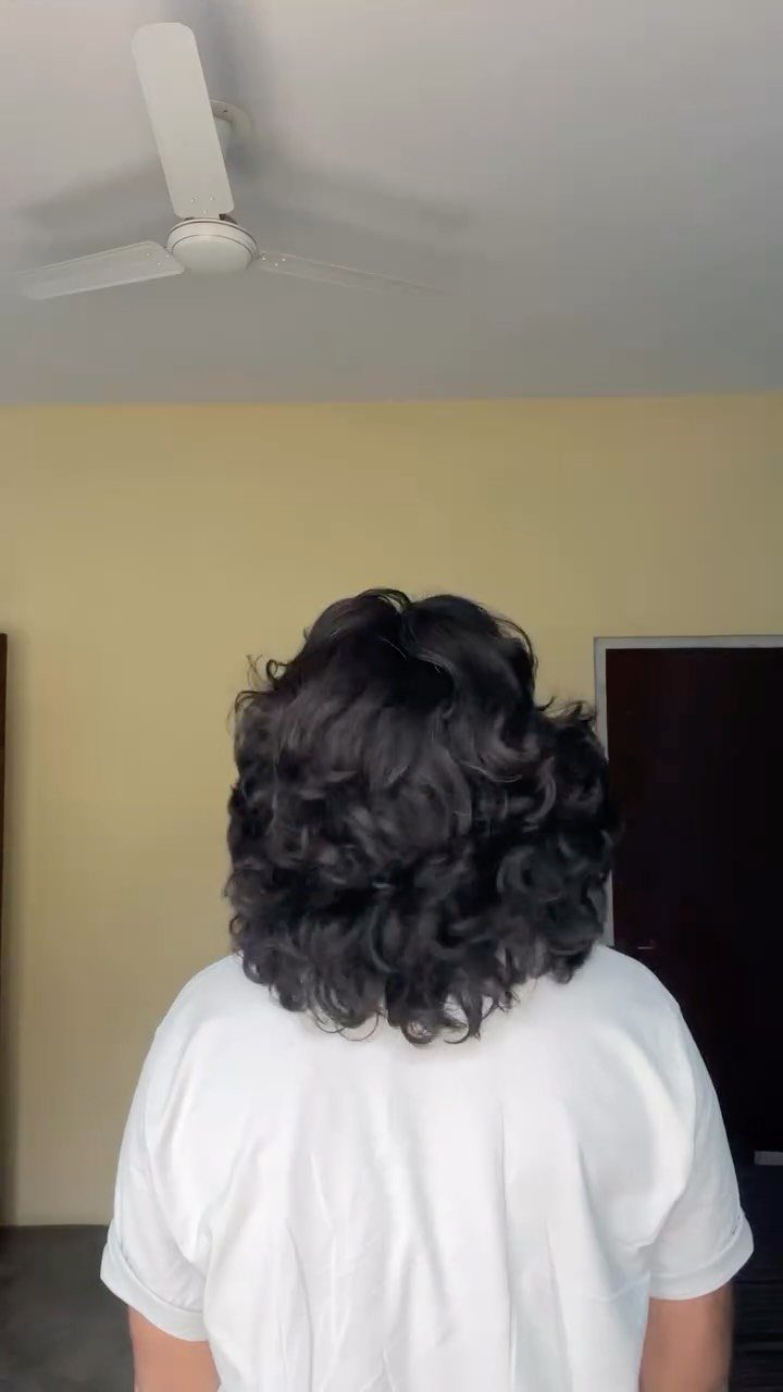 Man with long dark curly hair seen from behind wearing a white t-shirt