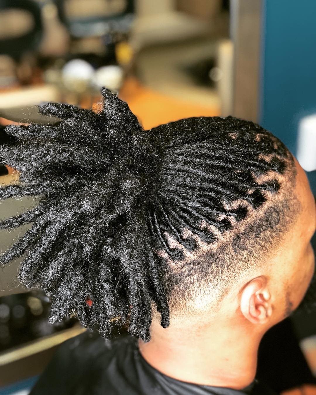 Man with black dreadlocks tied in a ponytail with a shaved undercut side.