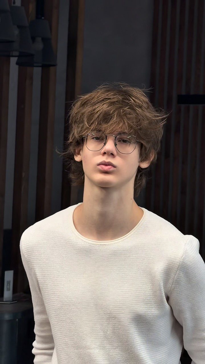 Young man with long brown hair and bangs wearing glasses and white sweater.