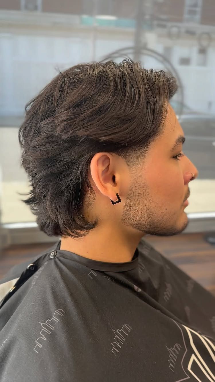 Man with long dark hair and tapered sides wearing a black barber cape