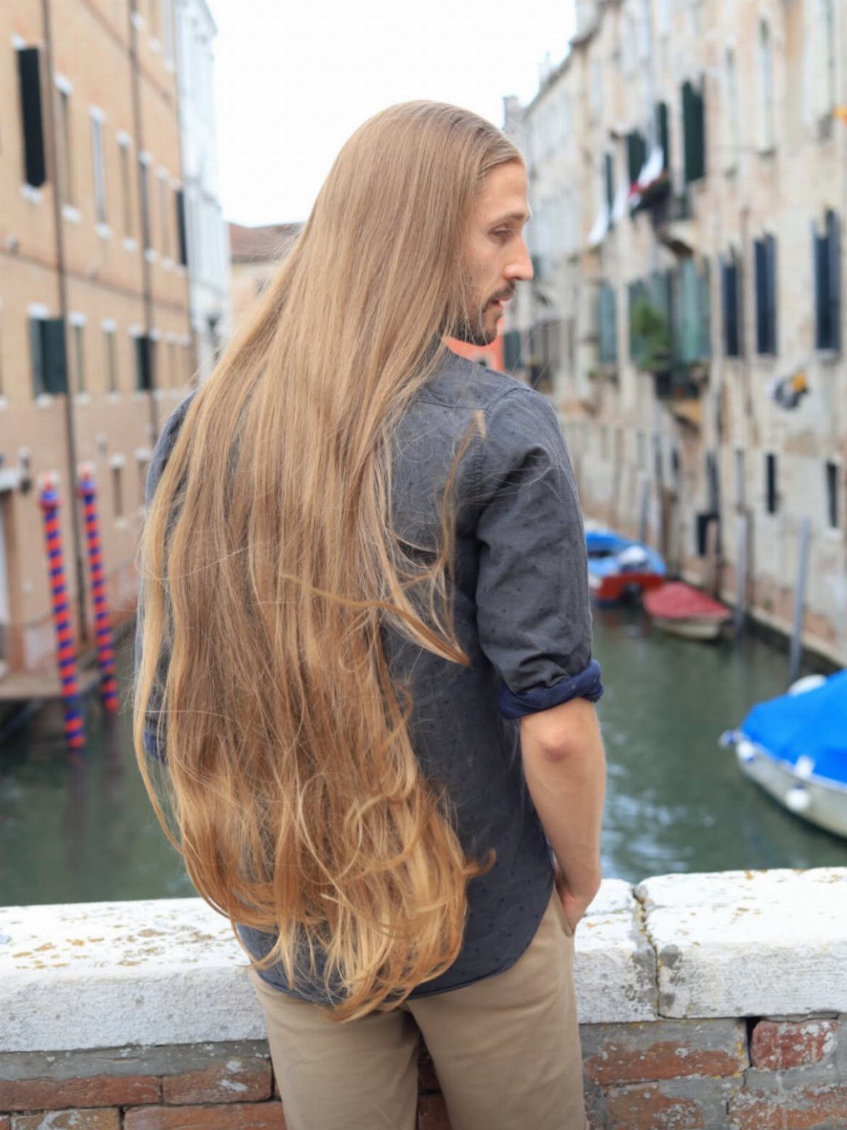 Man with very long straight light-brown hair standing by a Venetian canal