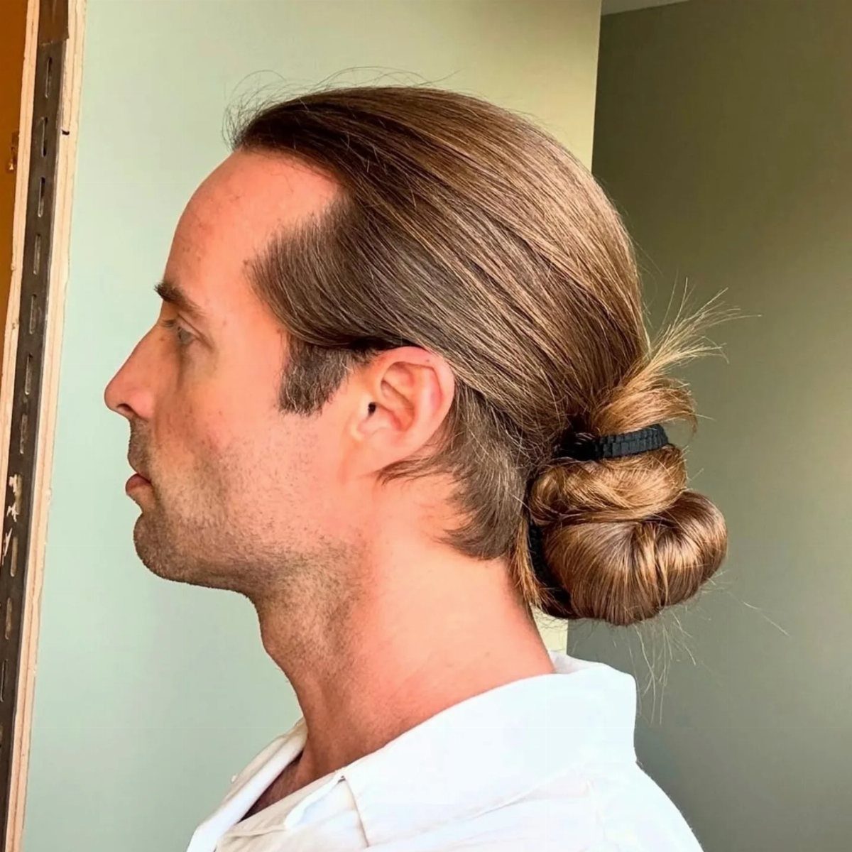 Man with light brown hair styled in a low twisted bun at the neck.