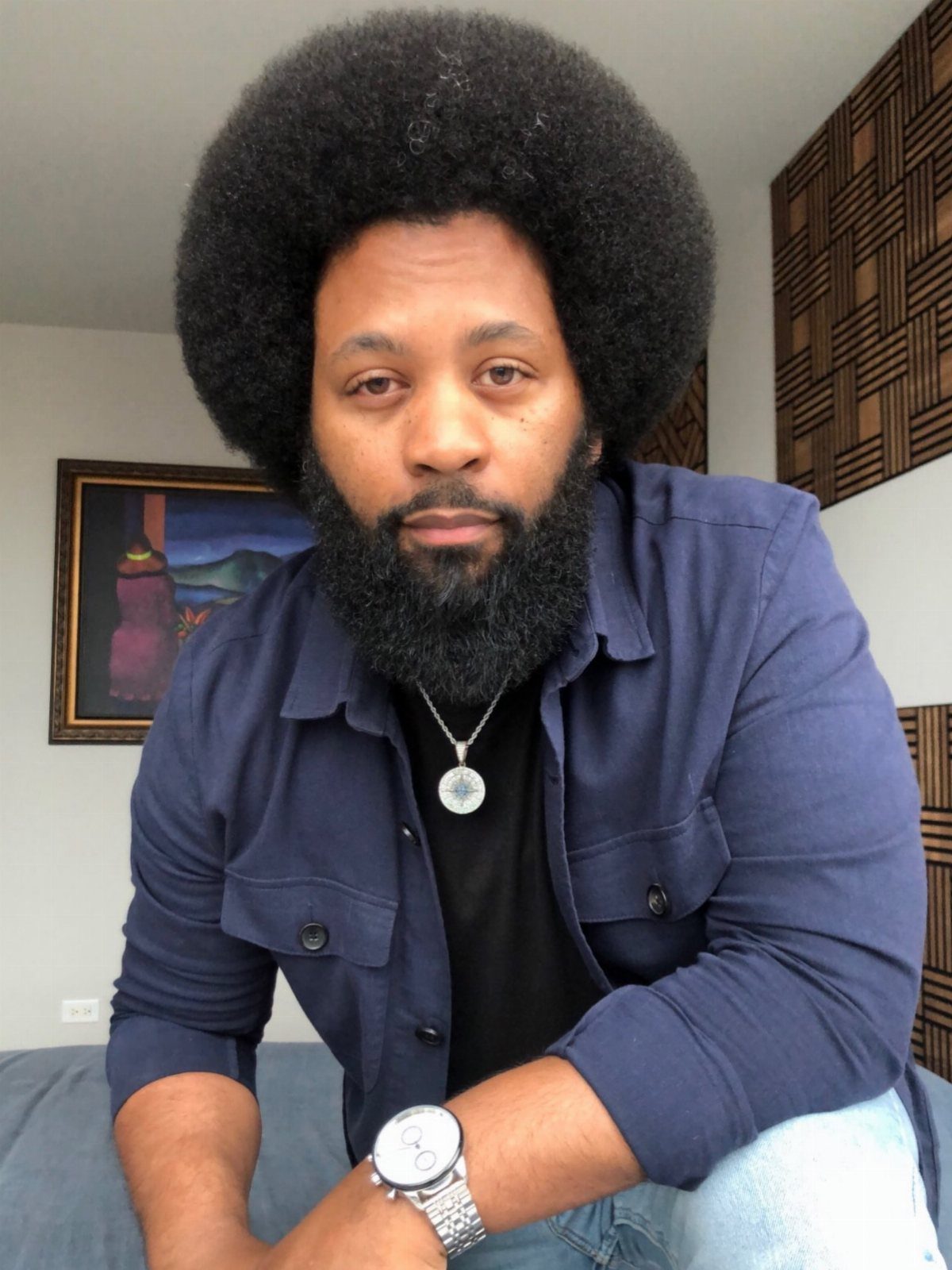 Man with a large rounded afro and full beard wearing a navy blue shirt.