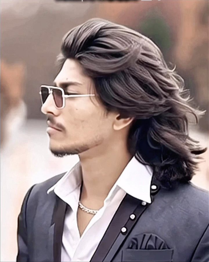 Man with long wavy brown hair wearing sunglasses and a black blazer.