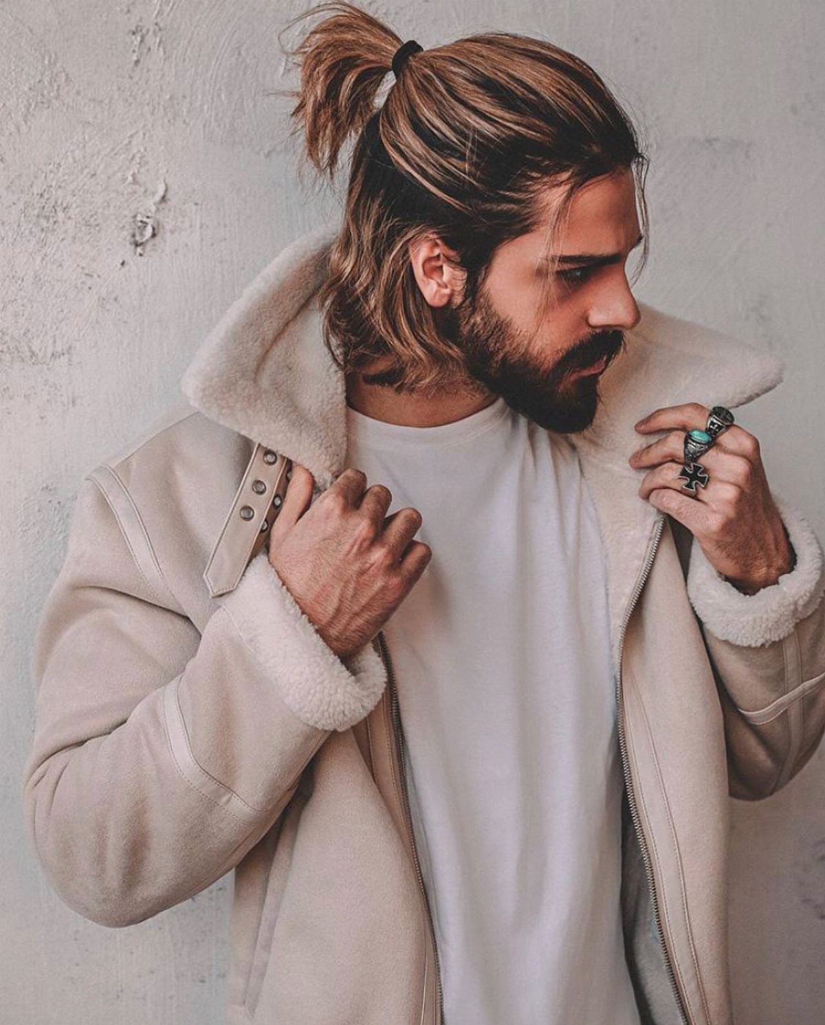 Man with long brown hair in a half-ponytail wearing a beige shearling jacket.