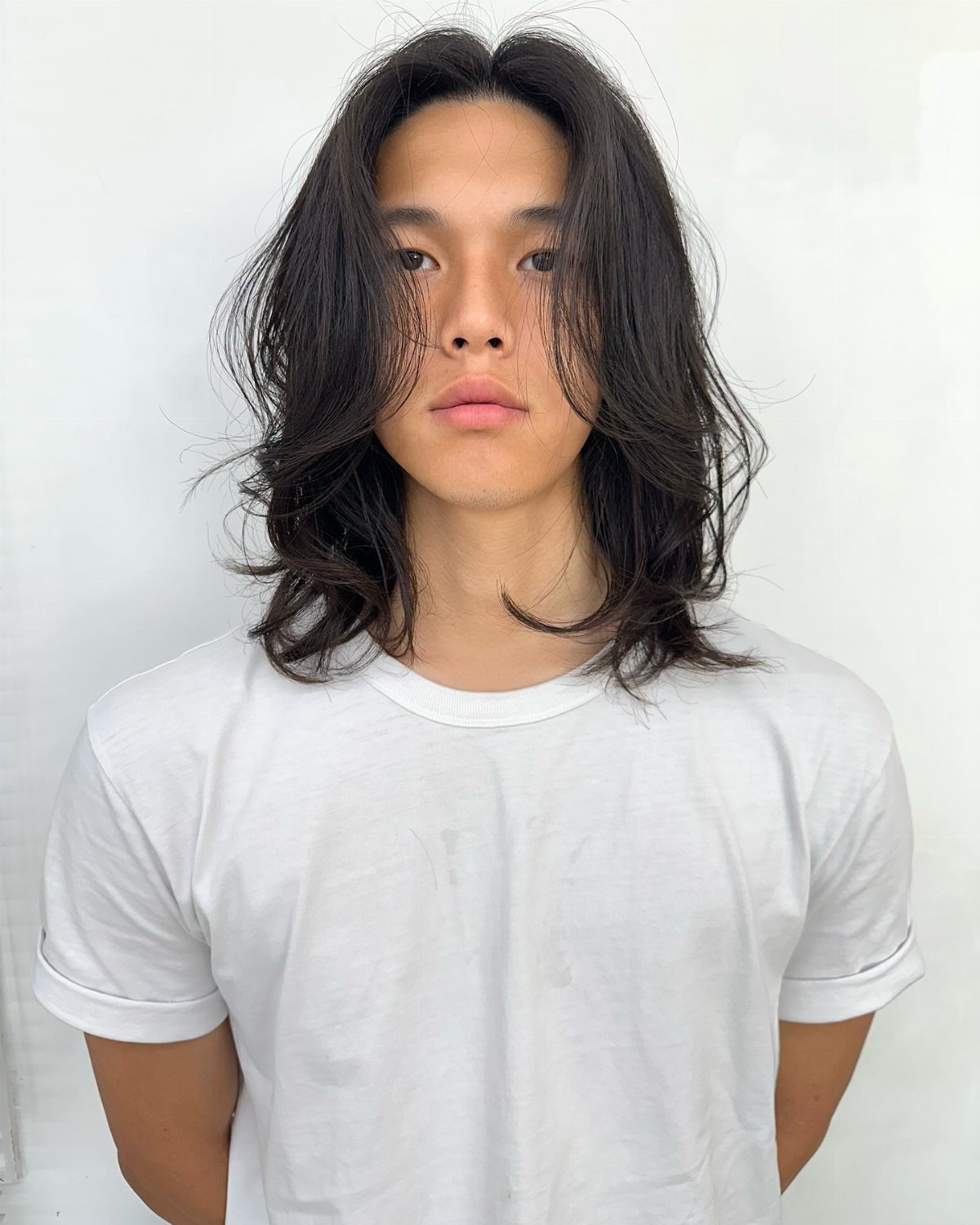 Young man with long dark layered hair and a white t-shirt.