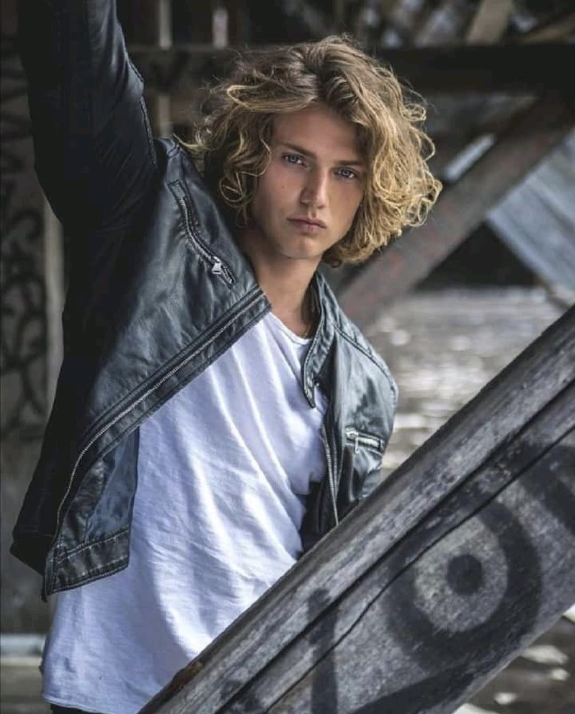 Young man with curly blonde shoulder-length hair wearing a black leather jacket.