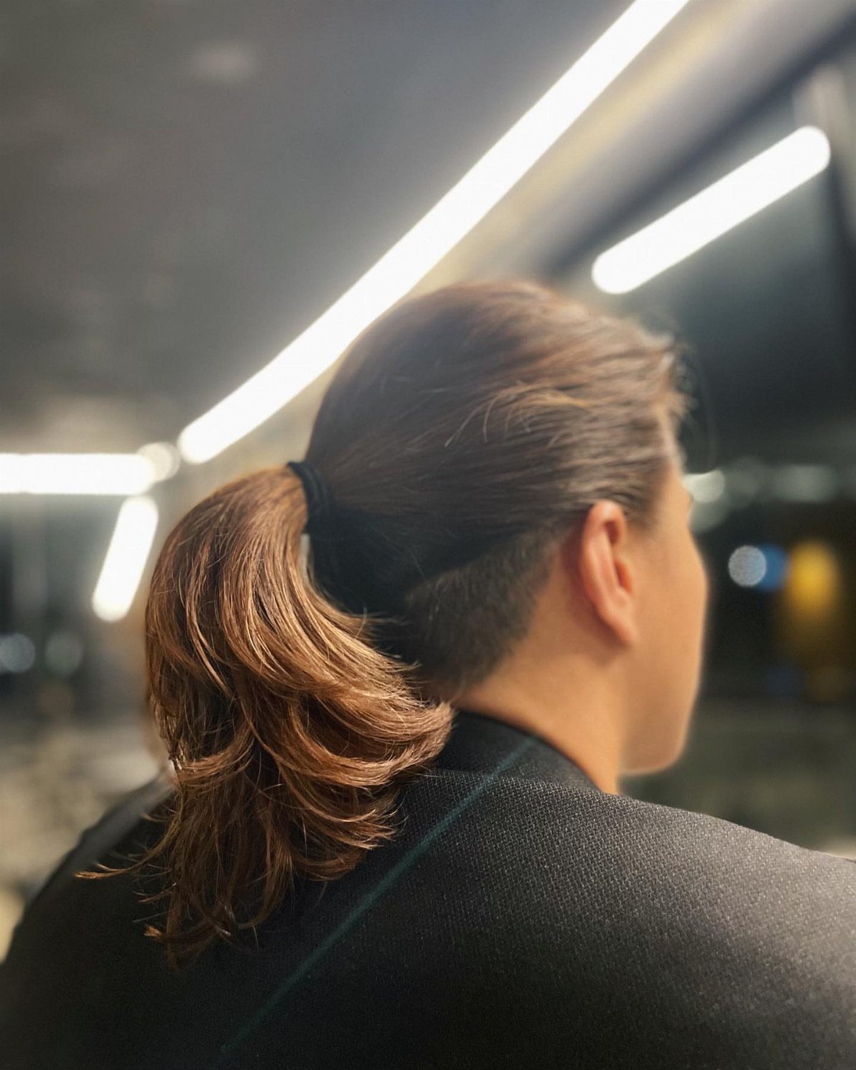 Man with brown hair tied in a ponytail wearing a dark blazer.