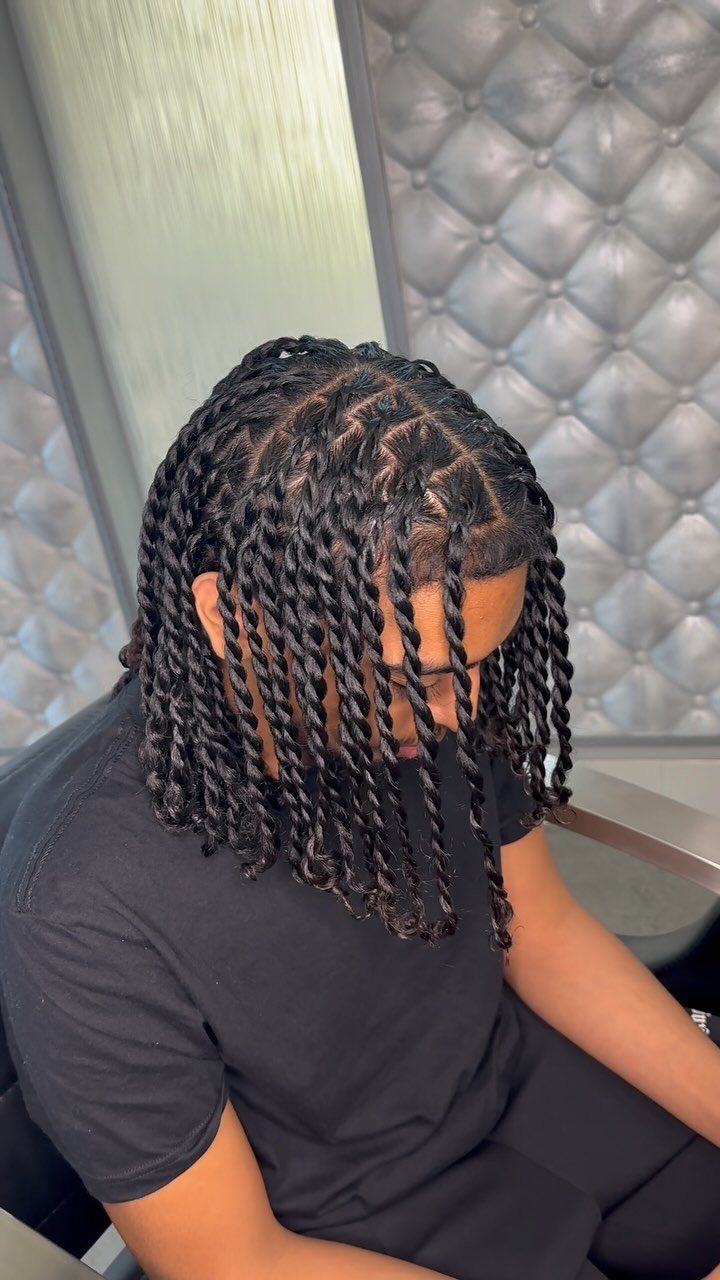 Man with long black twisted braids falling to his shoulders against grey wall.