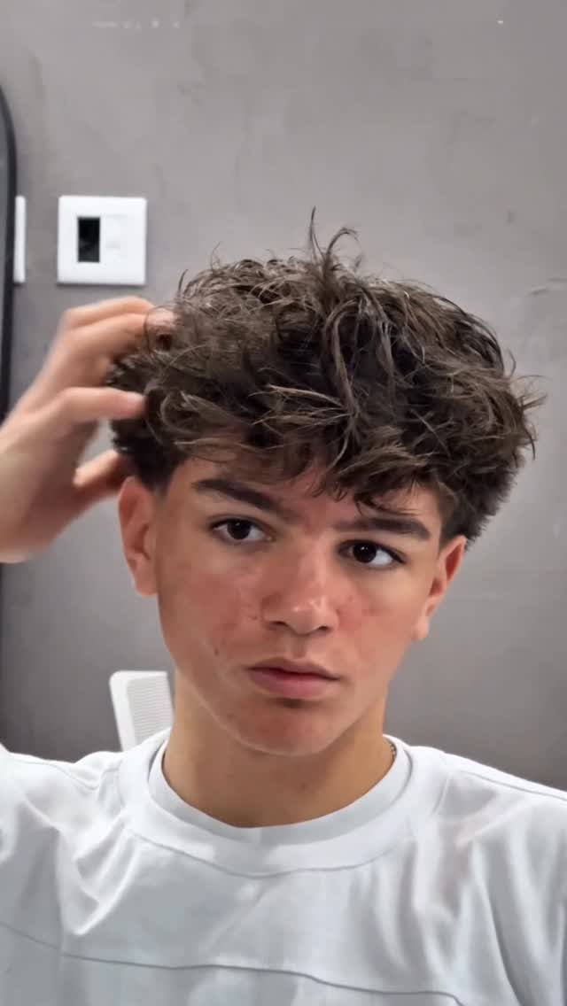 Young man with a curly broccoli haircut and faded sides wearing a white shirt.