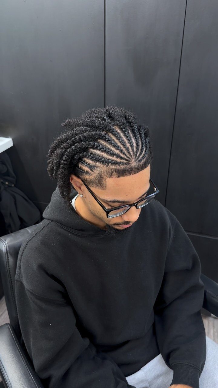 Man with cornrow braids styled straight back, wearing glasses and a black hoodie.