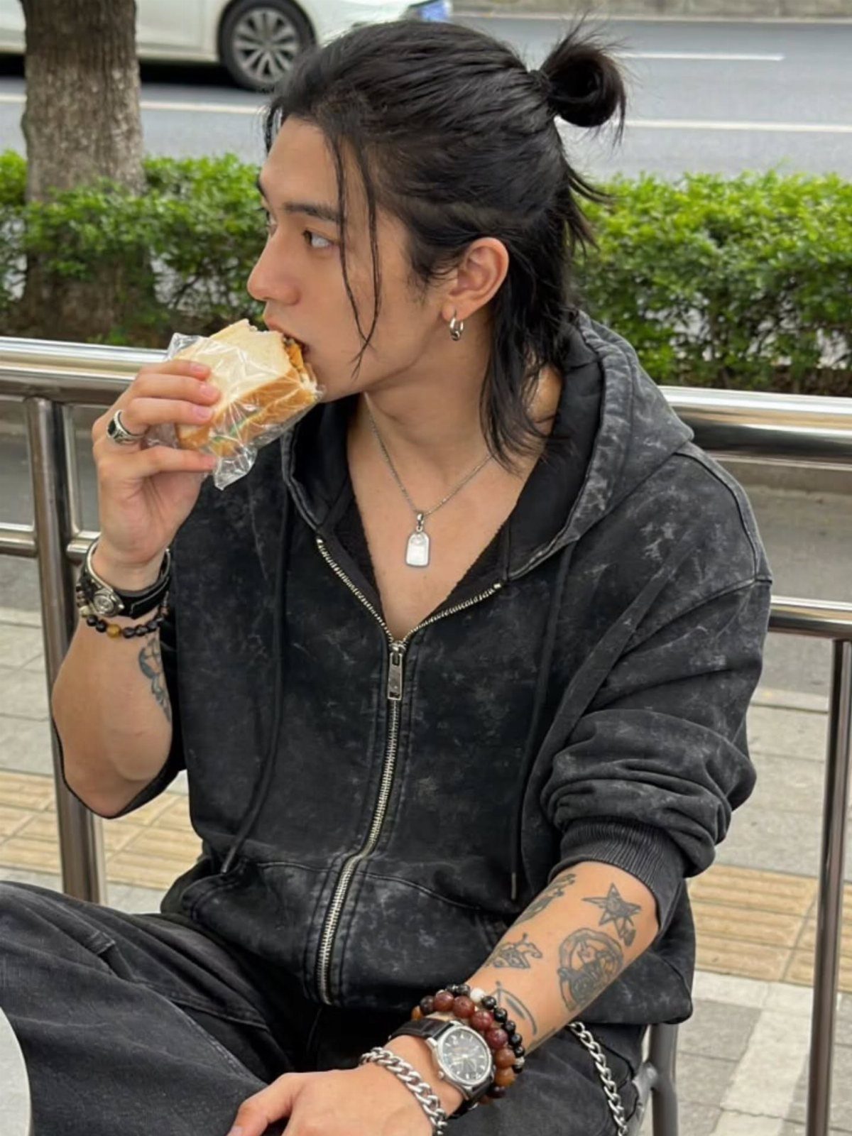 Man with a half-up man bun and loose back hair eating a sandwich.