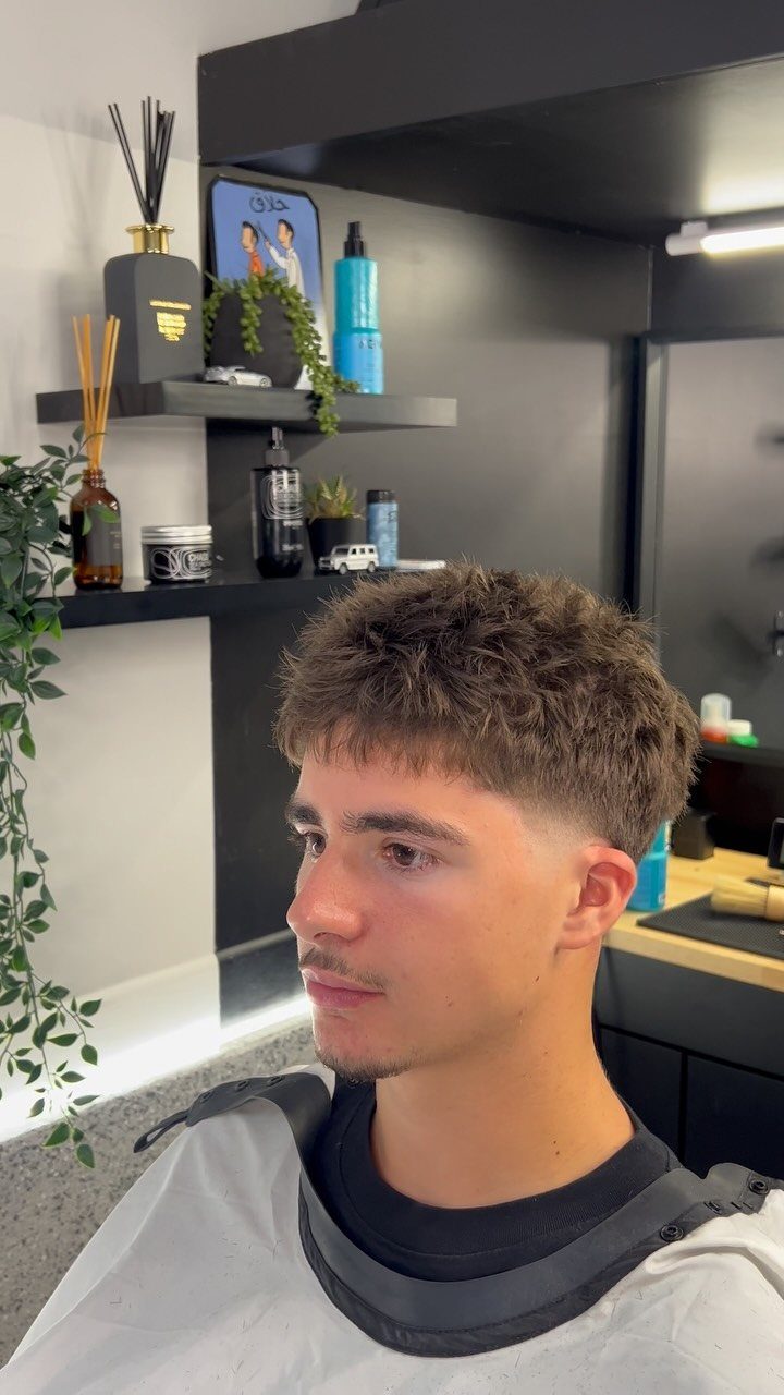 Young man with a textured medium length brown hairstyle and faded sides in salon