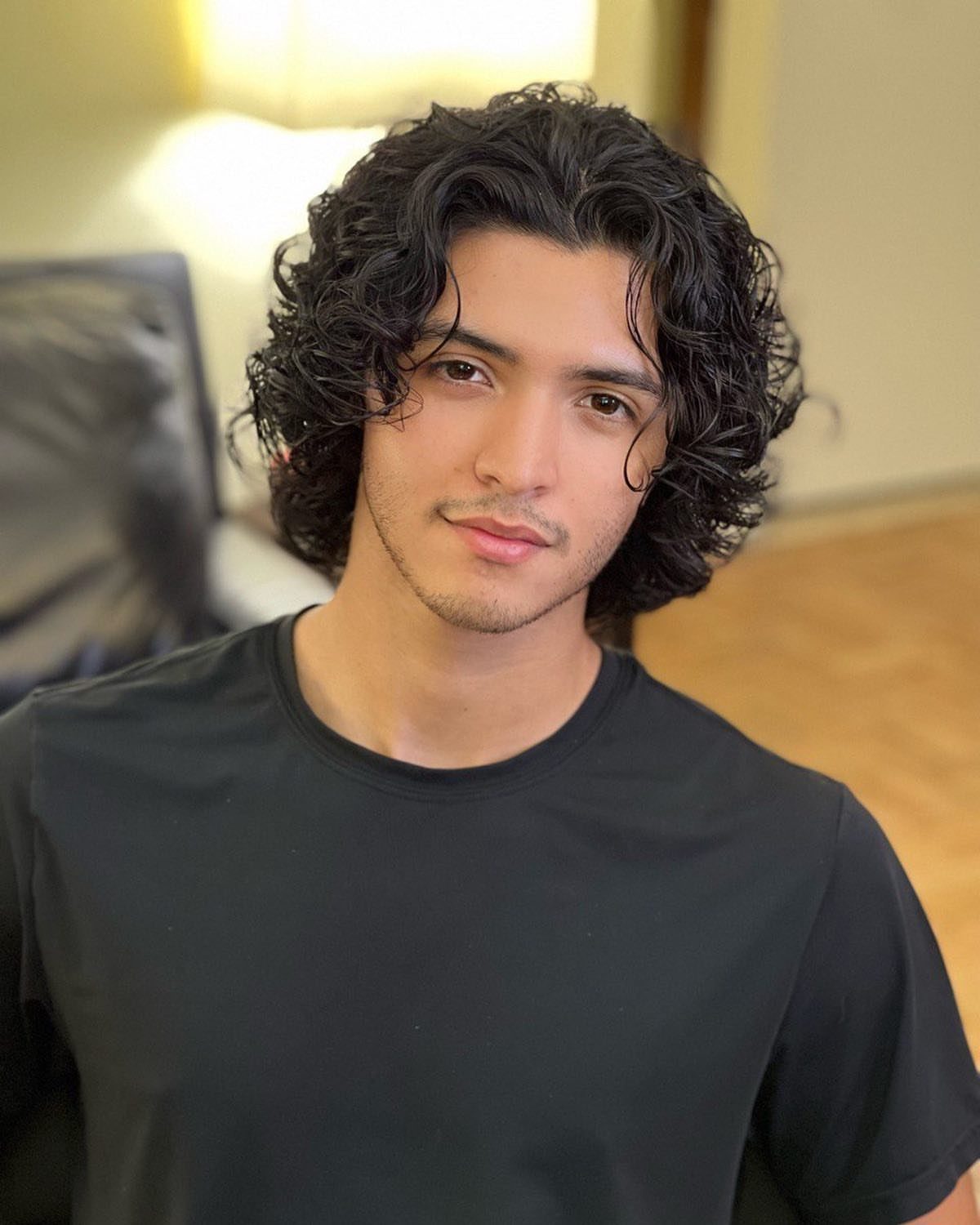 Young man with medium-length curly dark hair wearing a black t-shirt.