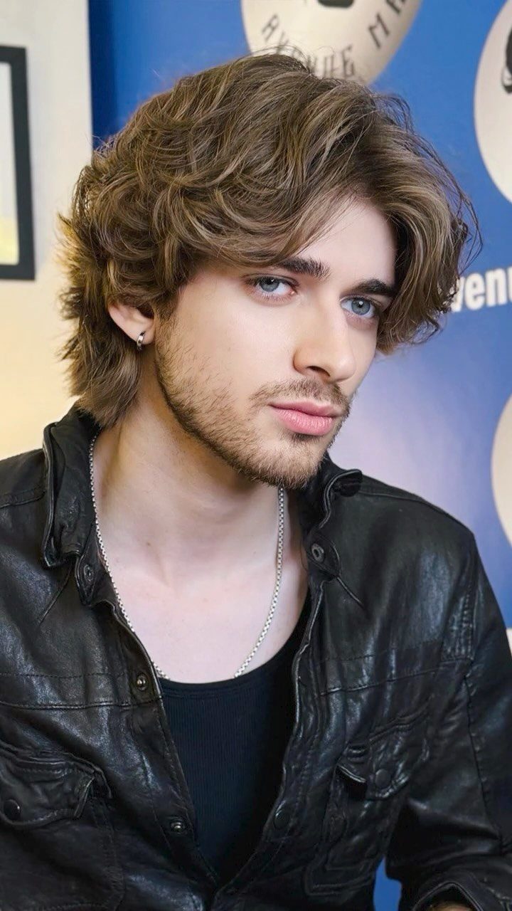 Young man with medium length layered light brown hair and a short beard.