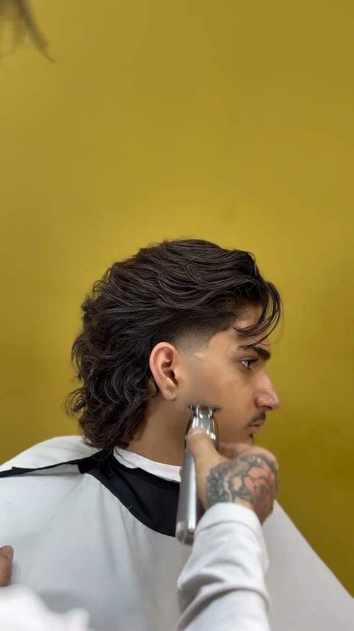 Man with a medium-length mullet hairstyle getting a trim from a barber.
