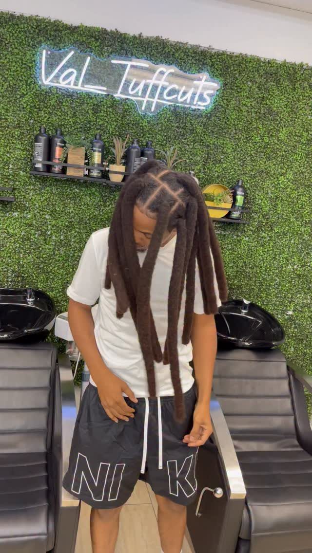 Man with medium length brown locs posing in a modern barbershop setting.