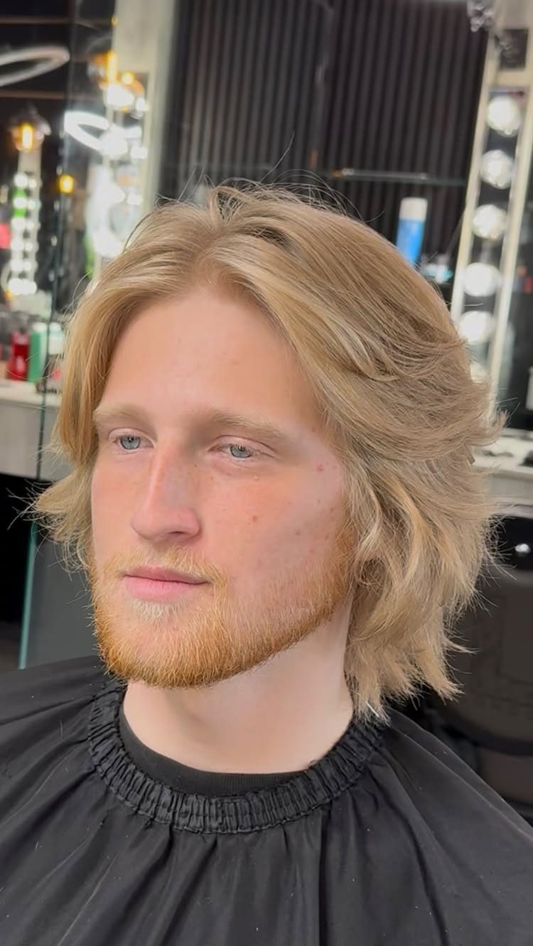 Man with blonde medium-length layered hair and a beard in a barbershop.