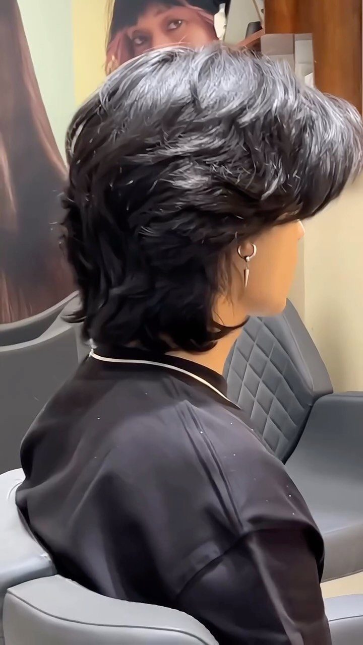 Person with a voluminous mid-length layered black haircut sitting in a salon chair.