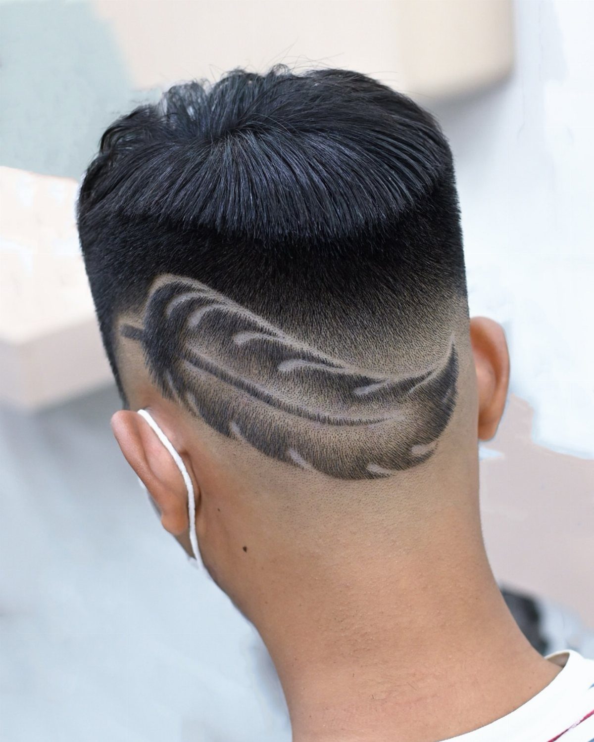 Man with a detailed feather design shaved into the back of his hair.