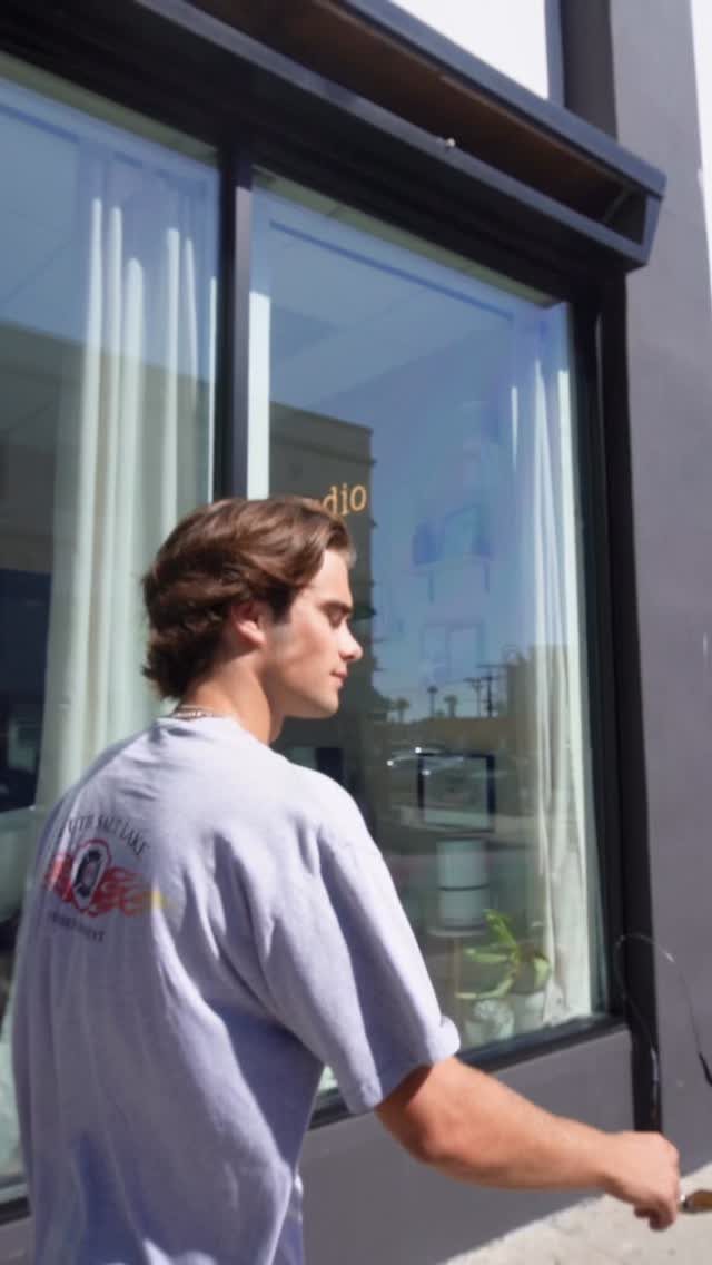 Man with wavy medium-length brown hair wearing a blue t-shirt outdoors.