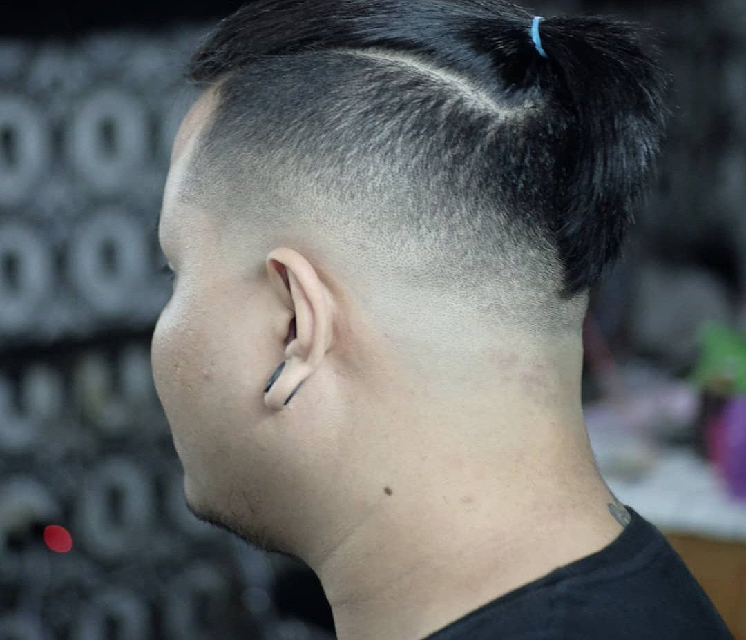 Man with a top knot hairstyle and high skin fade on the sides.