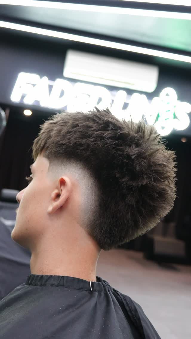 Young man with a burst fade haircut and textured spiky top in a barbershop.