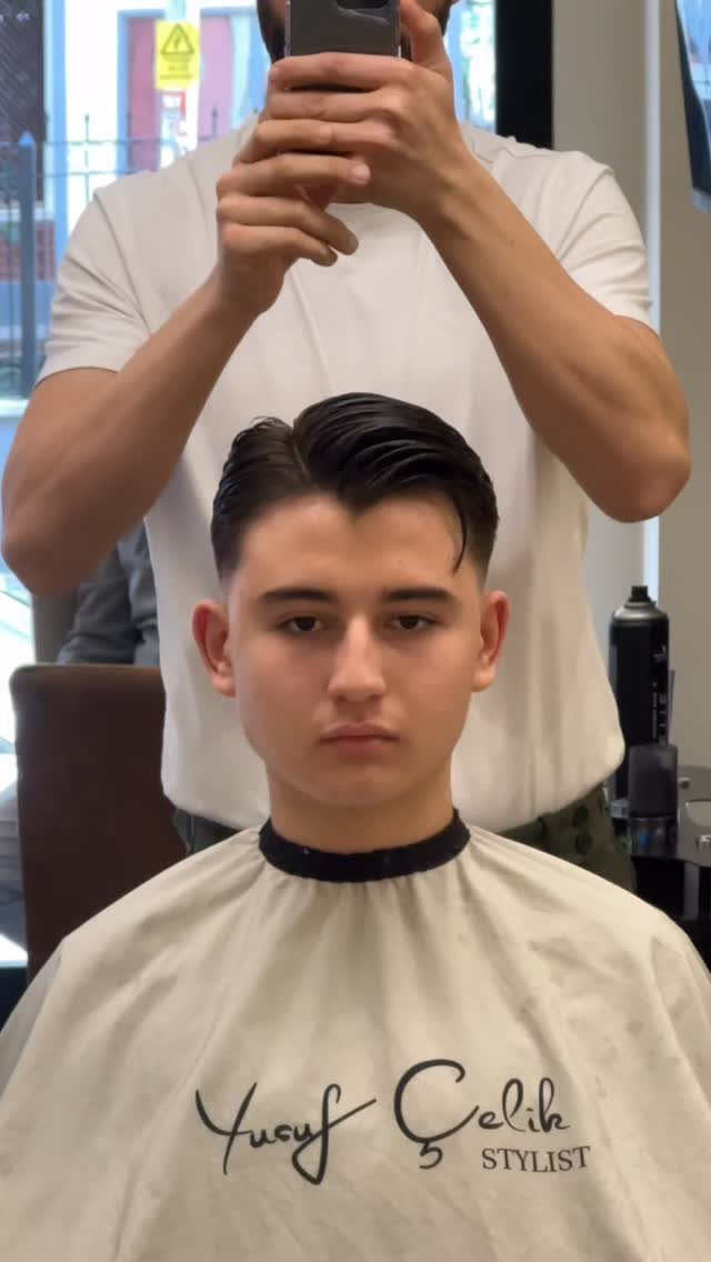 Young man with a comb over haircut and side part wearing a barber cape.