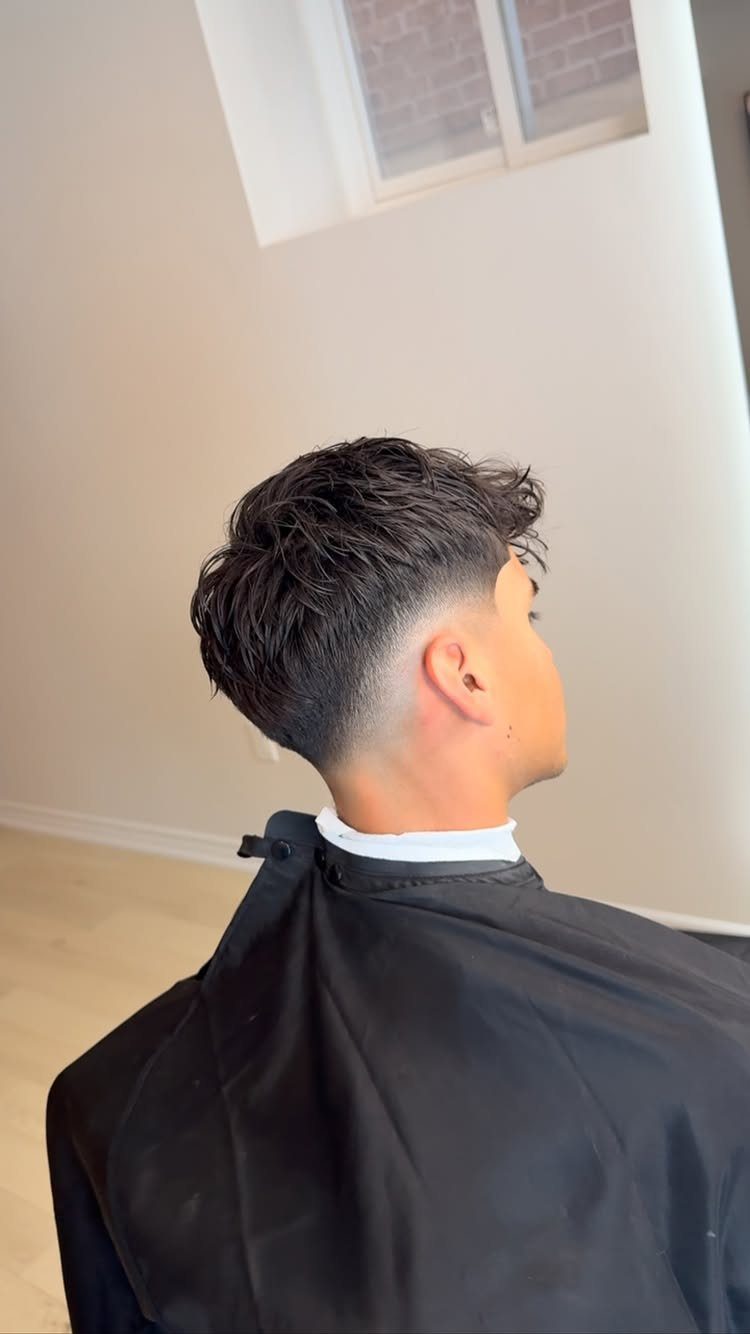 Man with a drop fade haircut and wavy top wearing a black cape.
