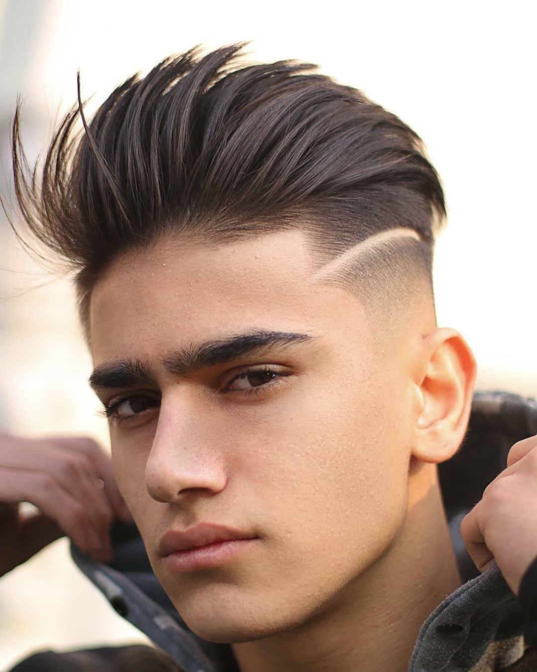 Young man with a mid fade haircut, brushed up top and shaved side design.