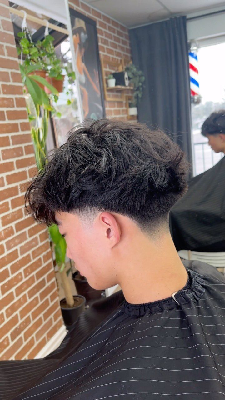 Young man with a mid fade haircut and textured wavy dark hair on top.