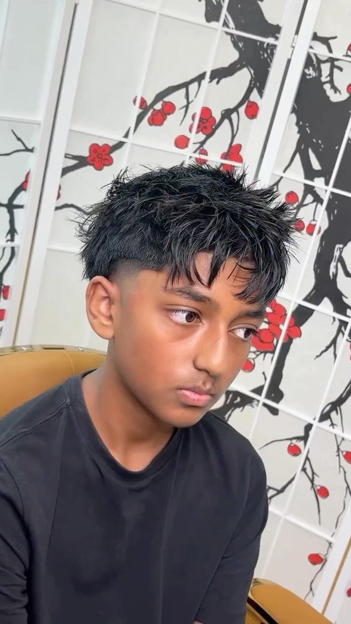 Young man with a mid fade haircut and textured fringe over his forehead.