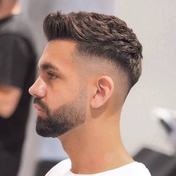 Man with a mid fade haircut and a styled quiff on top with a beard.