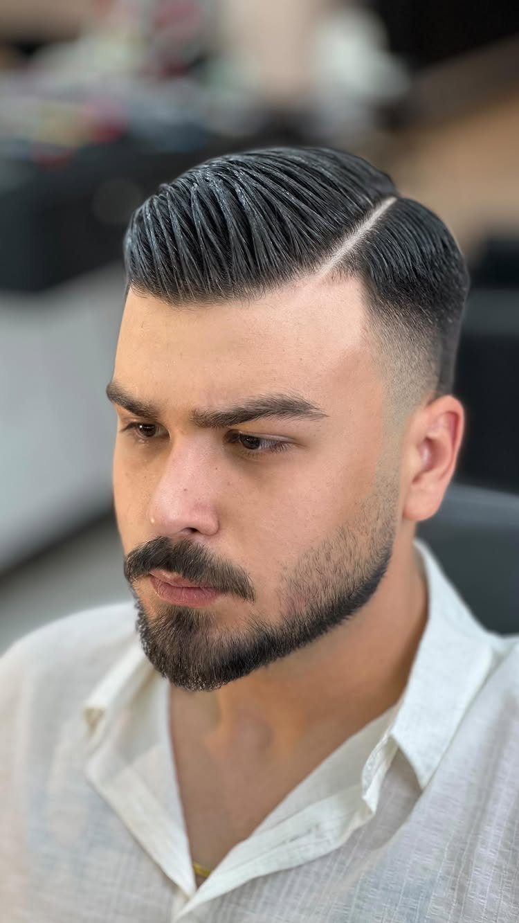 Man with a side part haircut, mid fade, and a well-groomed beard.