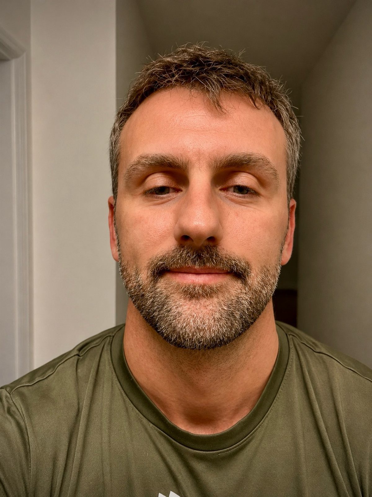 Man with a neatly trimmed full beard and mustache wearing an olive green shirt.