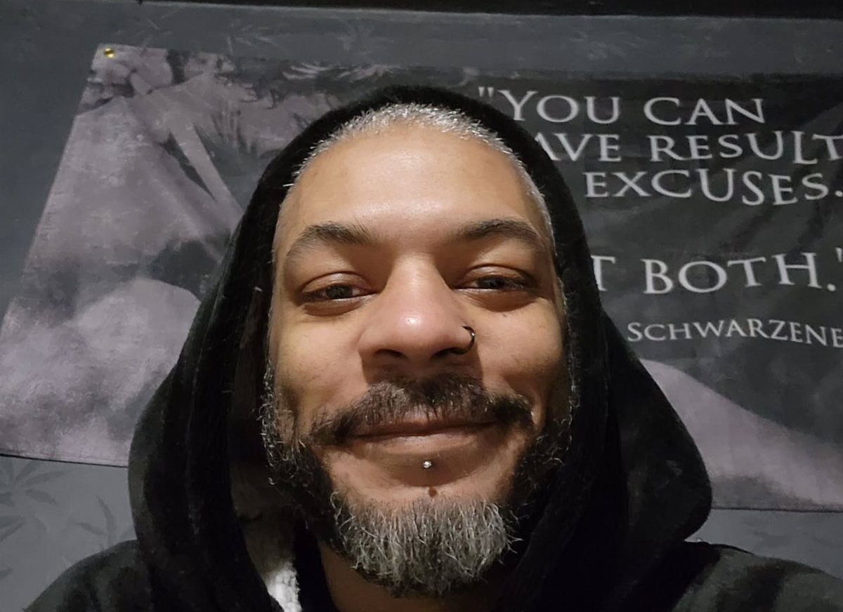 Man with grey hair and a mustache and goatee wearing a black hoodie.