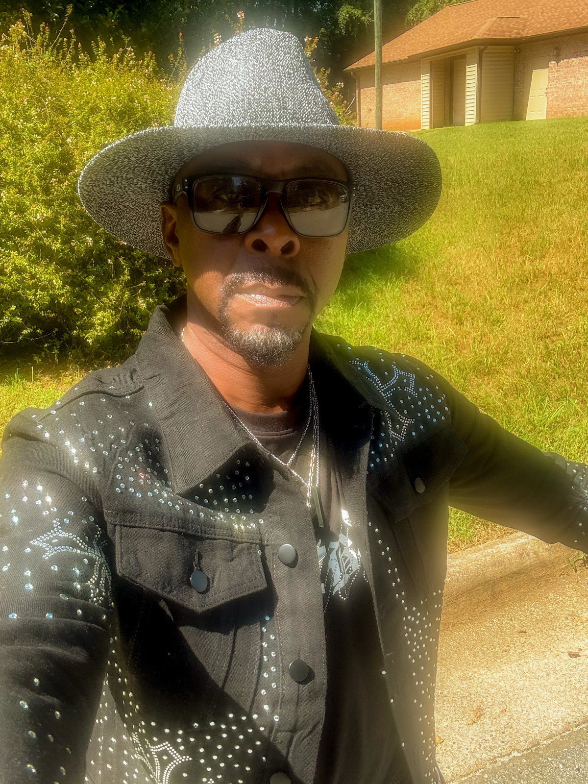 Man with a trimmed mustache and goatee wearing a silver glittery hat and sunglasses.