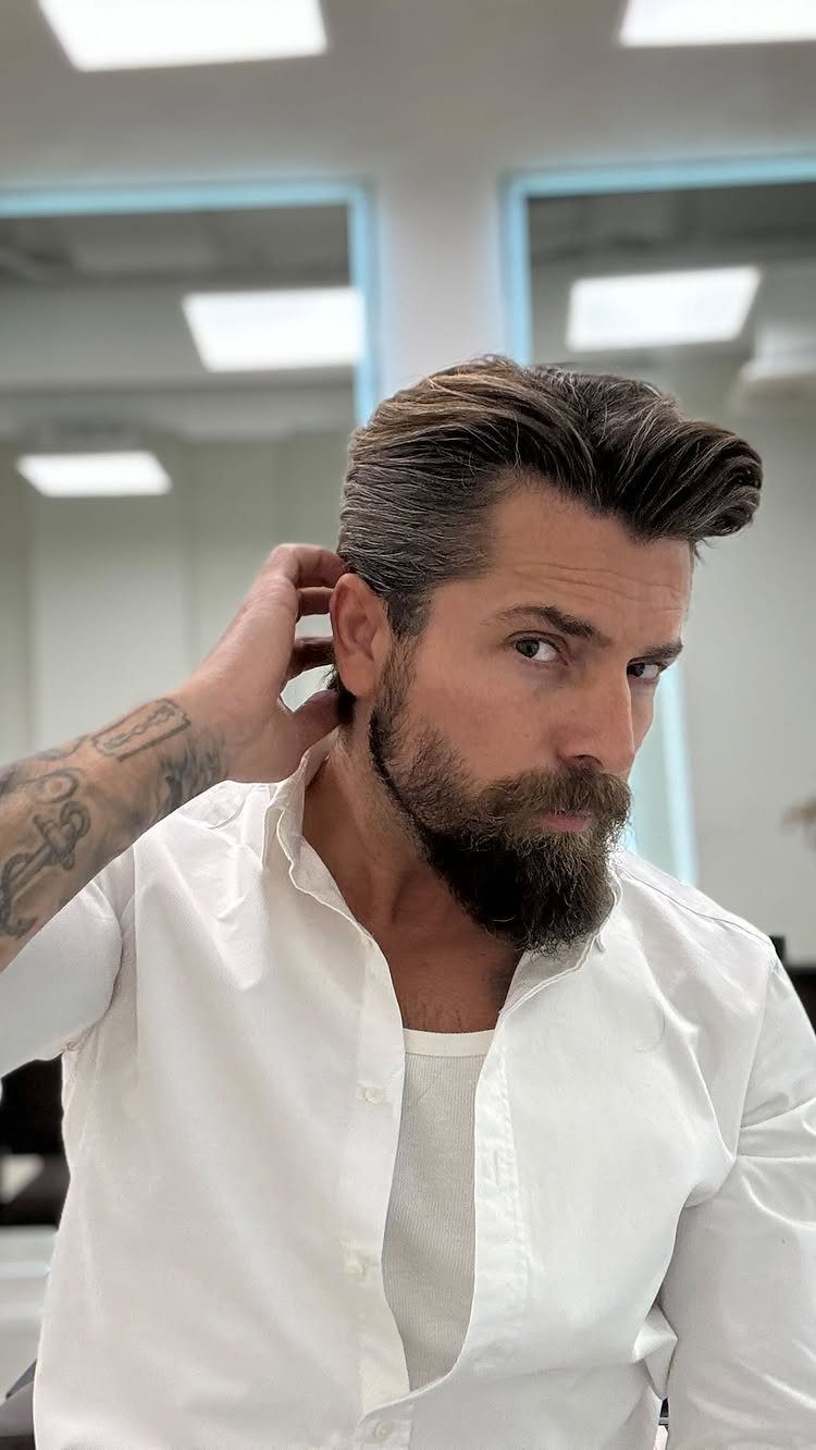 Man with a groomed beard and brown hair styled in a brushed back look.