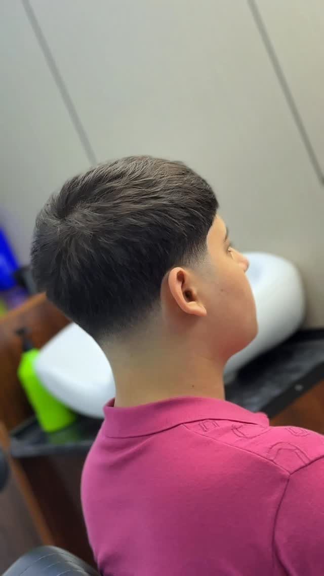 Young man with a short tapered haircut and dark brown hair in a barbershop.