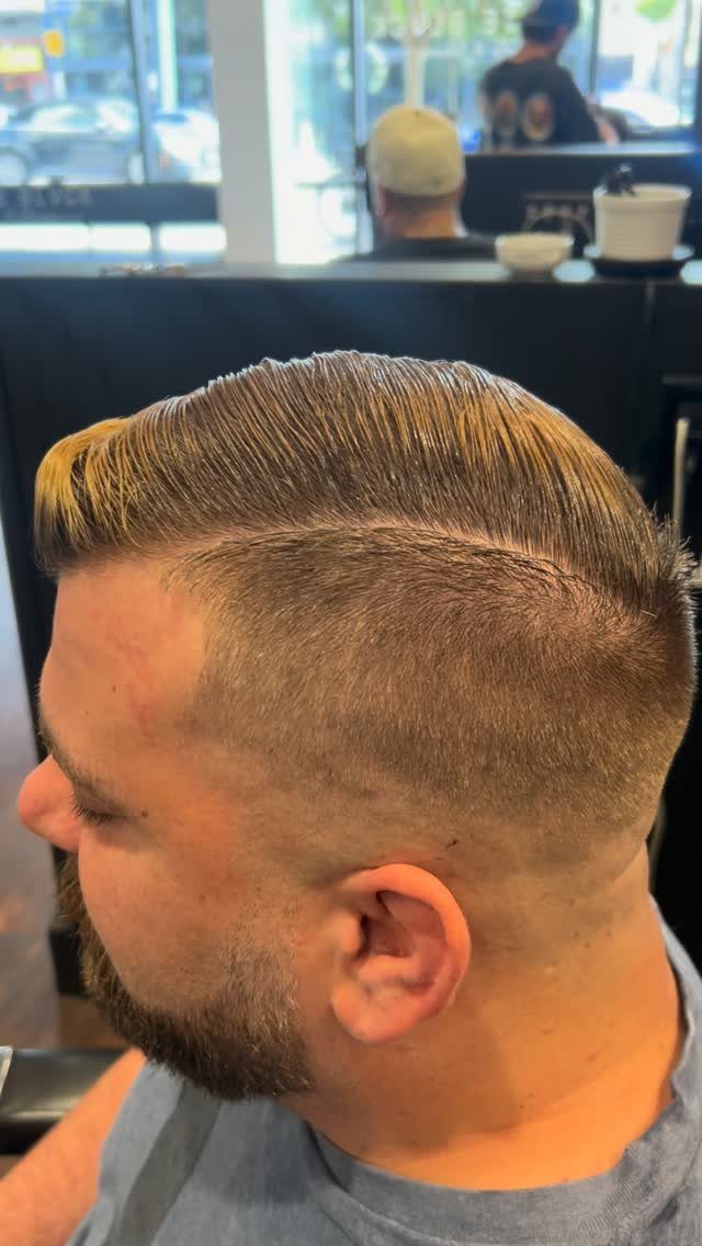 Man with a blonde comb-over haircut featuring a distinct shaved hard part and fade.