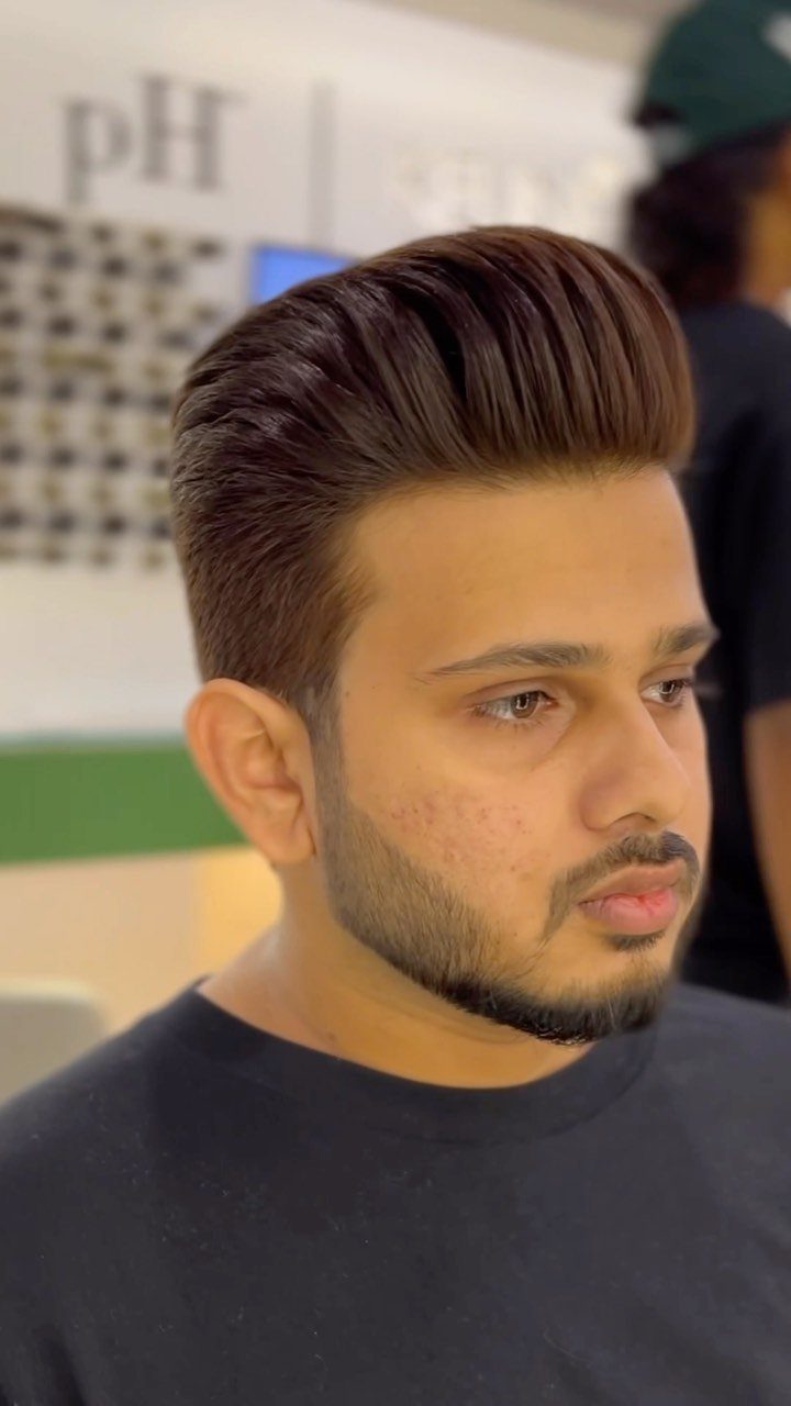 Man with a brown pompadour hairstyle and groomed beard in a barbershop.