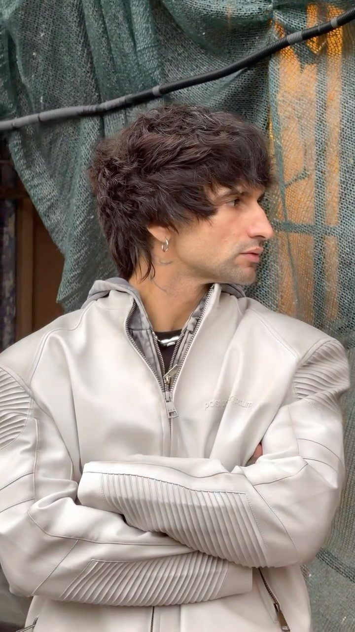 Man with shaggy dark hair and long bangs wearing a white leather jacket.