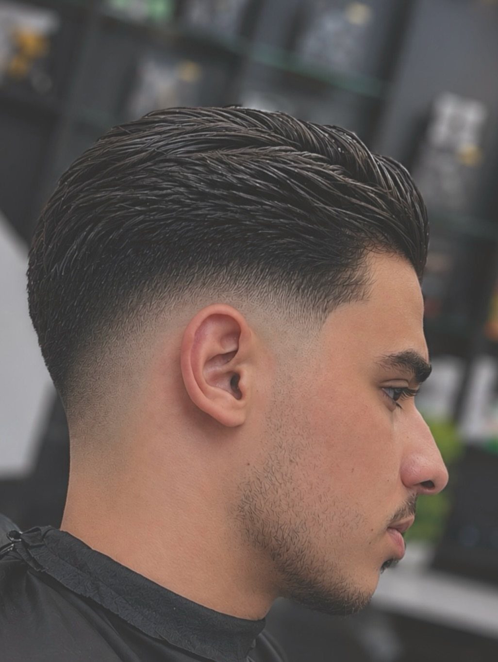 Man with a skin fade haircut and a textured, styled top in a barbershop.