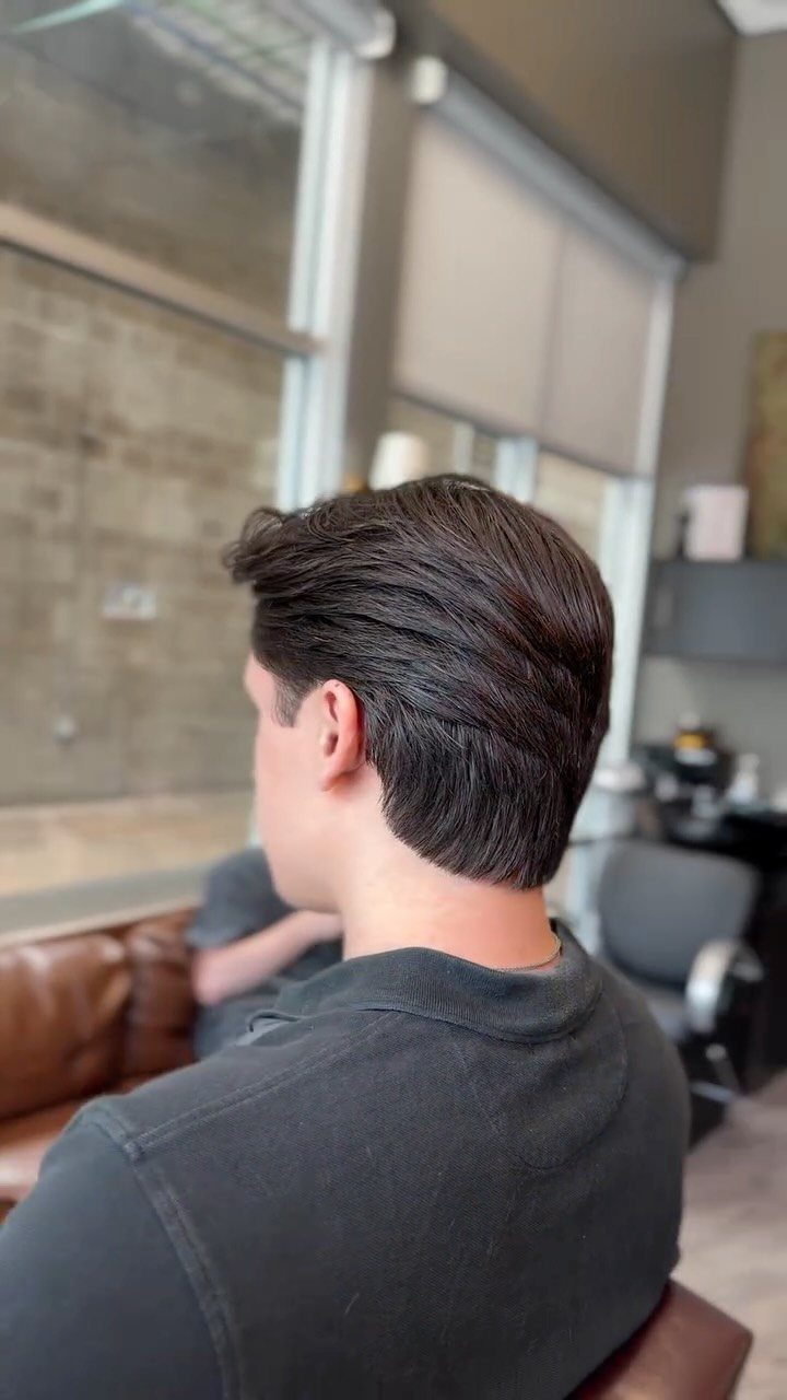 Man with dark straight hair styled in a slicked back look from behind.