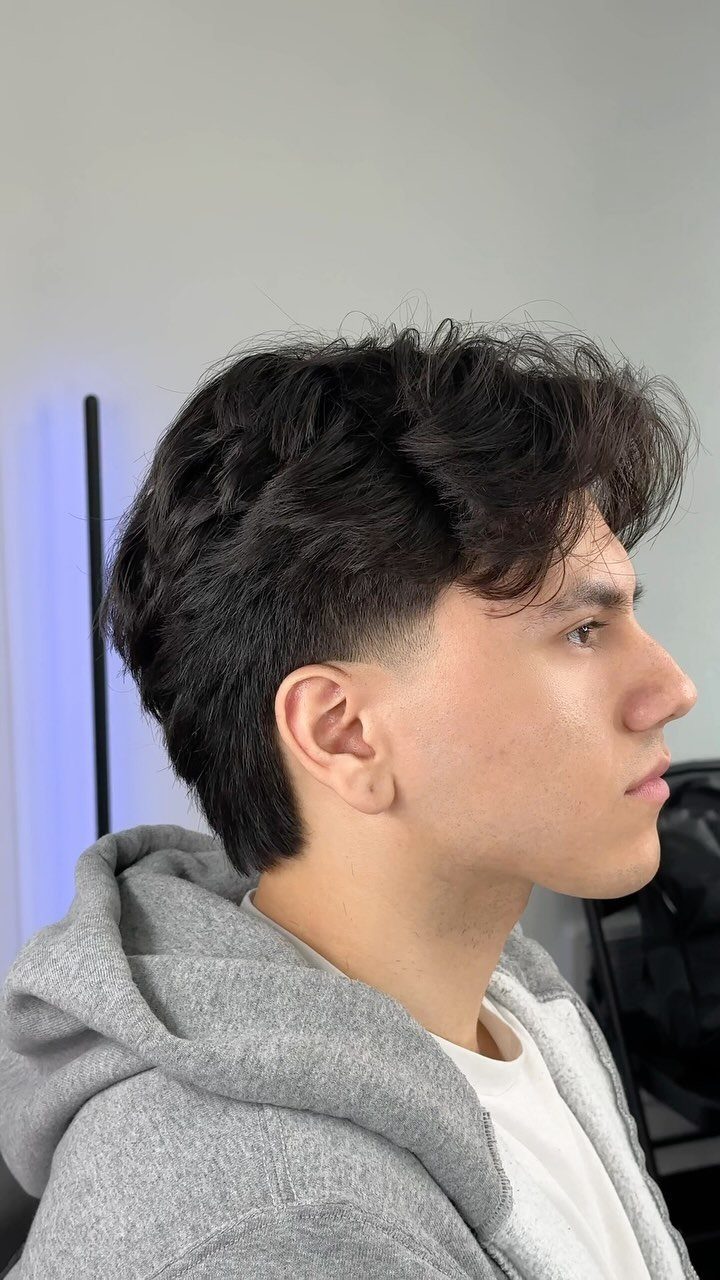 Young man with a textured short haircut and dark wavy hair in profile.