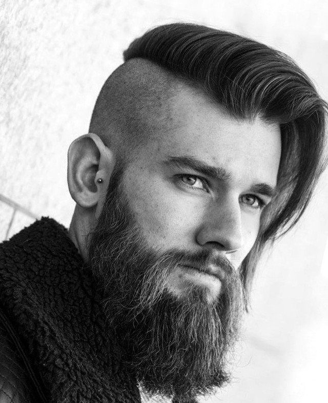 Man with a full beard and a side-parted undercut hairstyle in black and white.